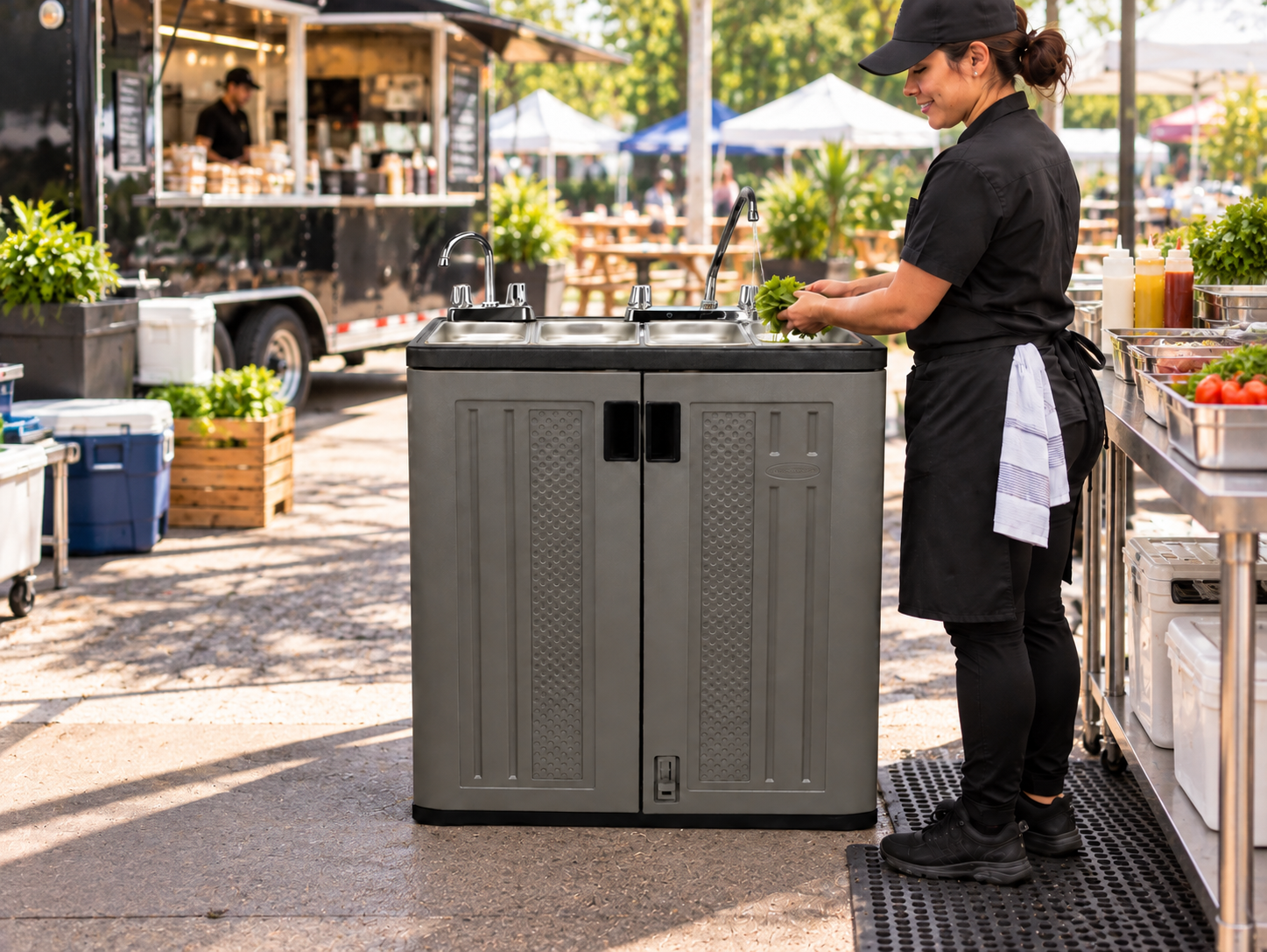 Food vendor washing lettuce at a portable multi-basin sink beside a food truck at an outdoor food festival.
